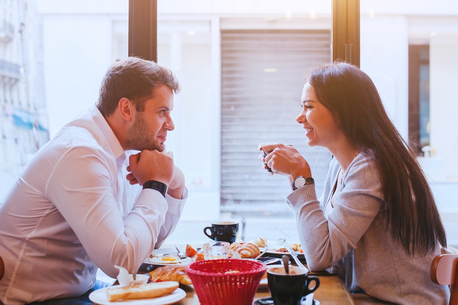 A couple leaning in and making eye contact over coffee and pastries at a cafe table.