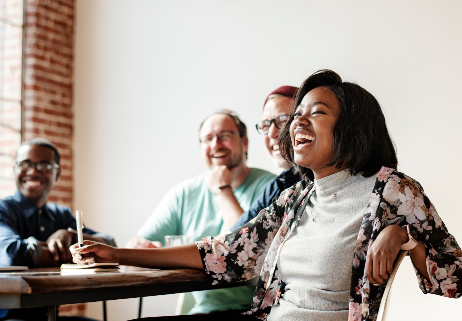 A group of coworkers laughing together around a table during a meeting.