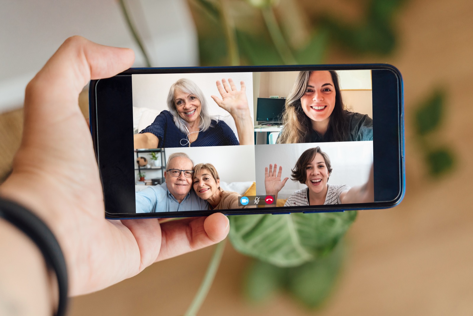 A woman holding up a phone during a family video call, with four relatives waving and smiling across the screen.