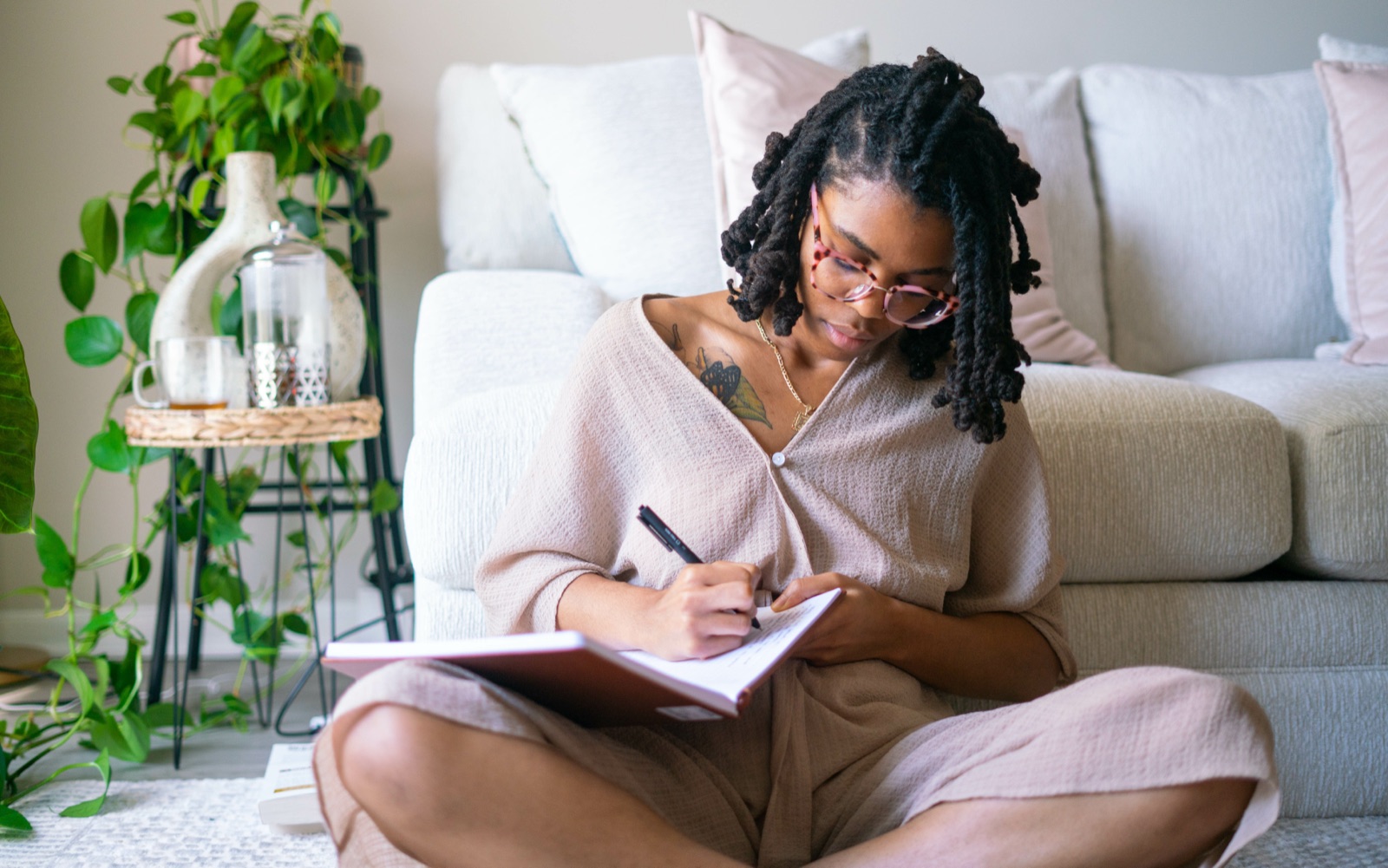 A woman sitting cross-legged on the floor in her living room, writing in a notebook.